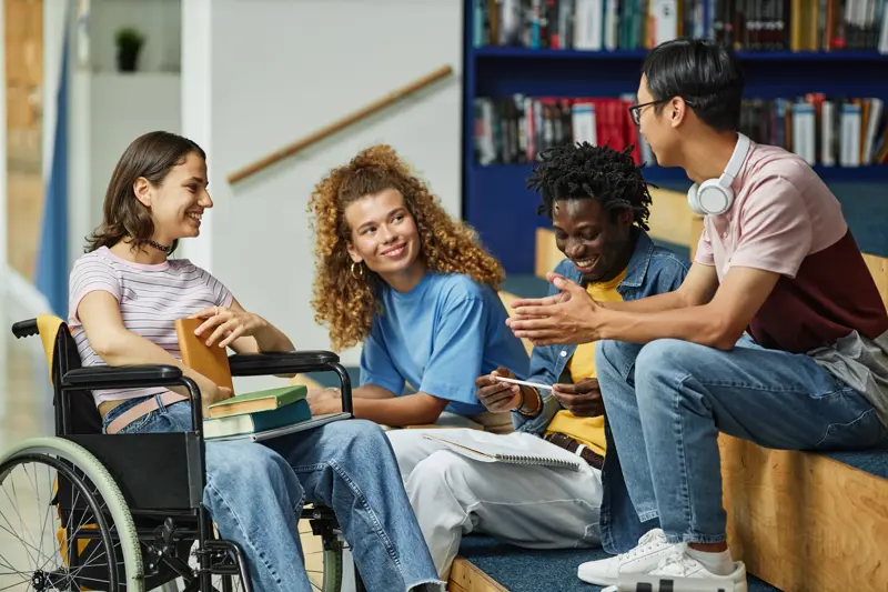 A student in a wheelchair with three other students sitting and talking